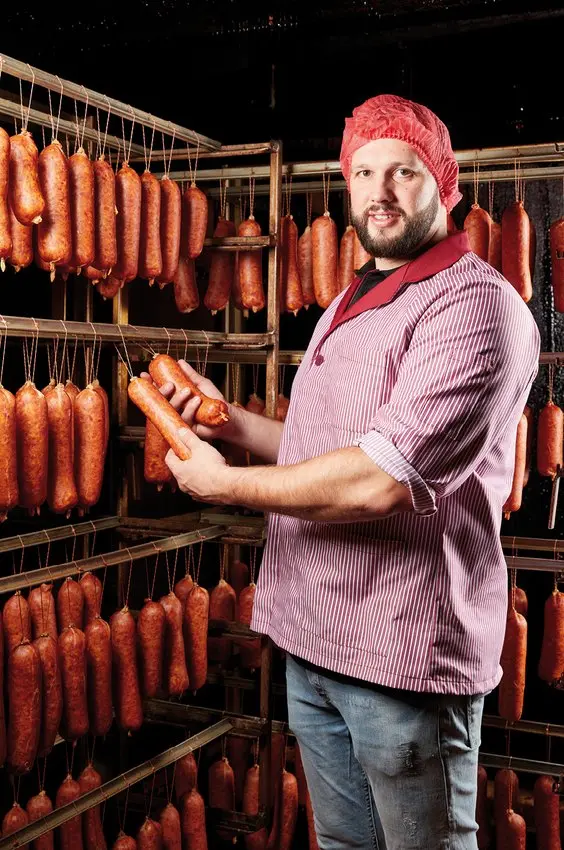Artisan présentant des saucissons dans un fumoir